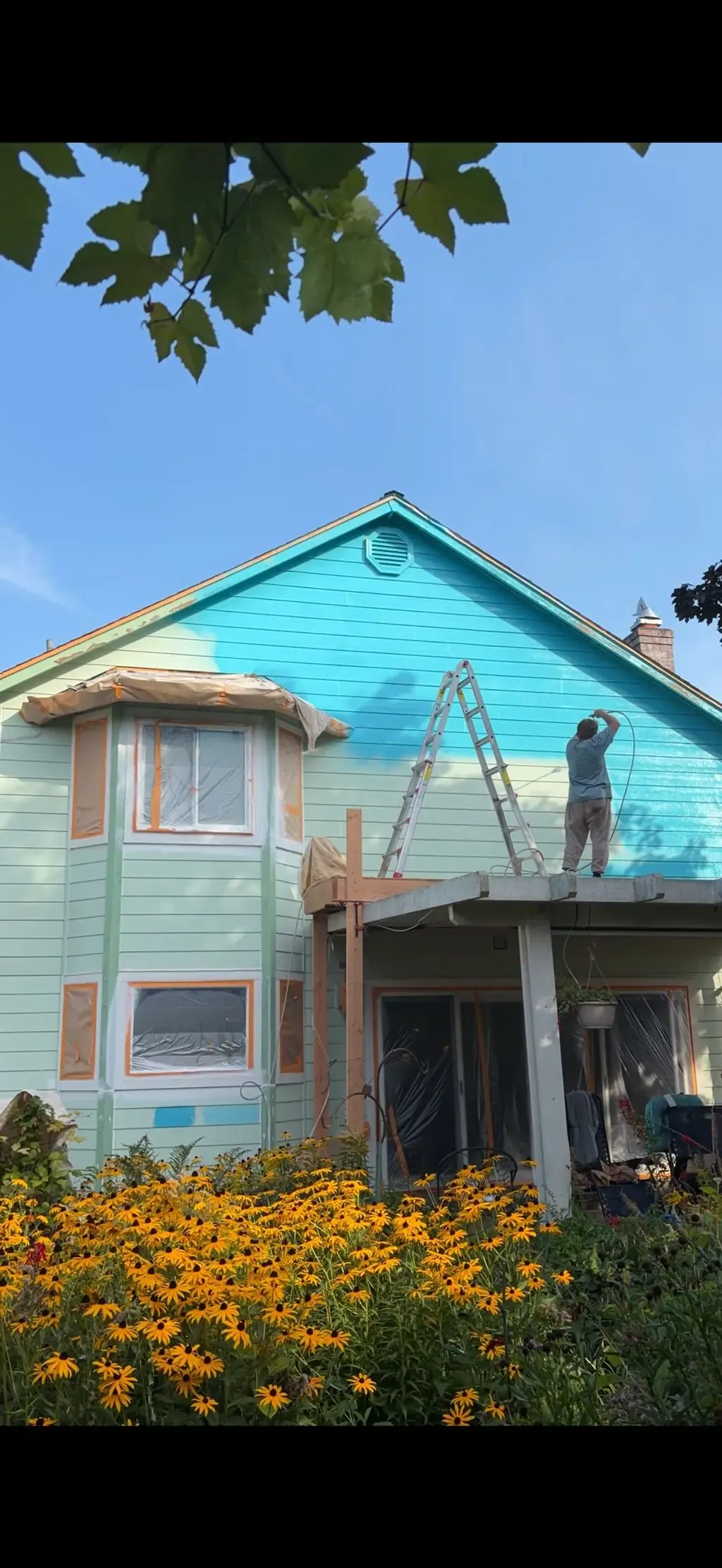 House exterior painting in progress with a painter on a ladder